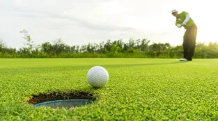 A golfer watches his putt from afar, as the ball rolls toward the hole on the green.